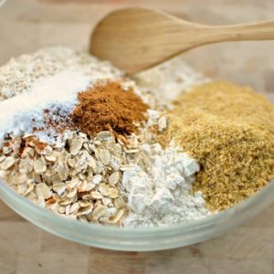 White dish with different piles of dry baking ingredients and a wooden spoon